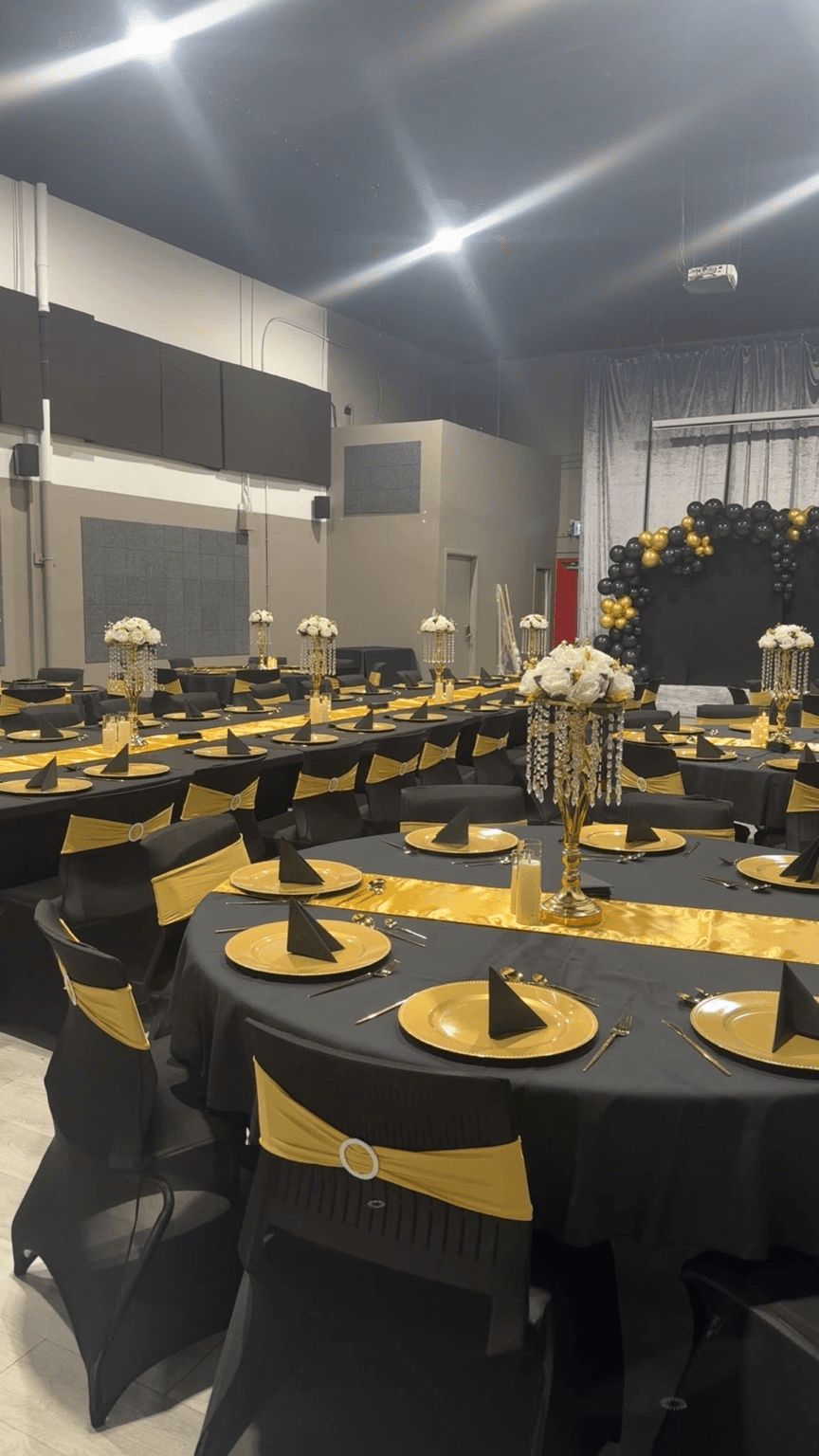 Reception tables with black linens, gold runners and chair sashes, and white floral centerpieces styled by Star Events