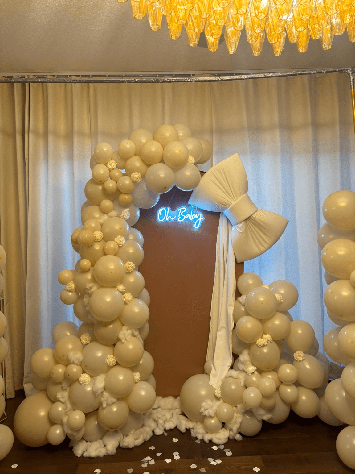 Baby shower backdrop with neutral balloons, floral accents, an ivory bow, and a glowing Oh Baby sign styled by Star Events